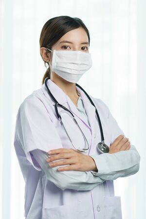 Portrait of a young woman doctor wearing medical mask with stethoscope in uniform.の写真素材