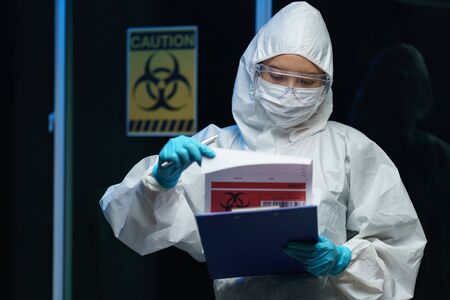 Coronavirus testing process: Woman Scientist wearing medical mask with safety glasses in hazmat suit, report with information about blood test.の写真素材