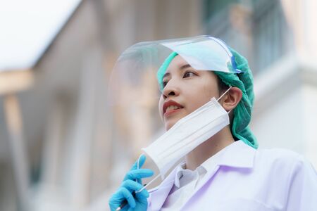 Woman doctor taking off a mask for take a break and holding patient report, outdoor portrait, Coronavirus COVID-19 pandemic.の写真素材