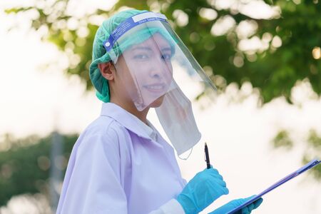 Woman doctor taking off a mask for take a break and holding patient report, outdoor portrait, Coronavirus COVID-19 pandemic.の写真素材