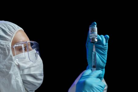 Woman in hazmat suit with vaccine and syringe injection for prevention, immunization and treatment from corona virus infection.の写真素材