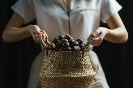 Person holding chestnuts on hand with wicker basket full of chestnuts.