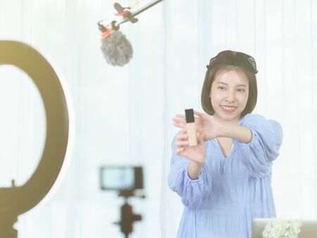 Woman vlogger holding skin care in hands, looking in camera while recording video for blog.の写真素材