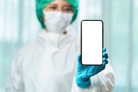 Doctor in hazmat suit (PPE) holding a smart phone with blank white screen for text. Coronavirus,...