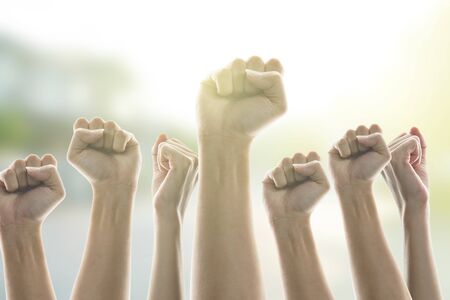People in city raised fists in the air,  sunlight background. victory and protest