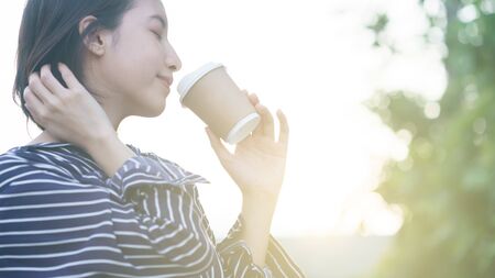 Woman holding paper coffee cup to take away in morning with sunlight.の写真素材