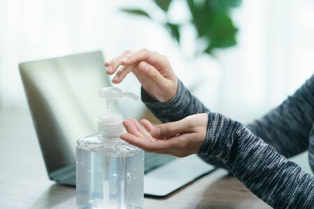 Woman worker wear protective face mask cleaning her hands with sanitizer liquid antibacterial gel, working from home in quarantine, corona virus concept.の写真素材