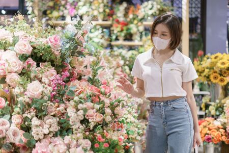 Woman wearing face mask chooses a flower at shop, during coronavirus pandemic.の写真素材