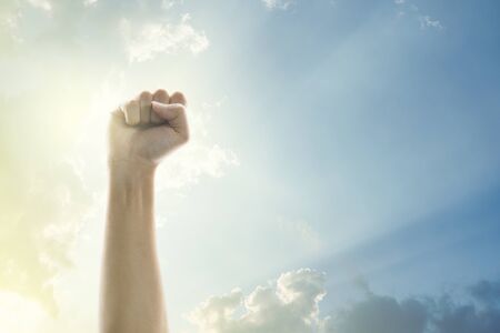 Fists of people raised in the air with clear sky and sunlight background.