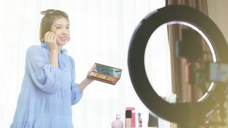 Woman vlogger holding eye shadow in hands, looking in camera while recording video for blog. makeup tutorialsの写真素材