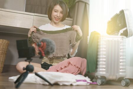 Woman blogger recording video about her clothing for travel with camera at home.の写真素材
