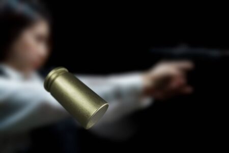 Flying bullet shells with Woman wearing bulletproof vest shoots with gun at a target at indoor gun...