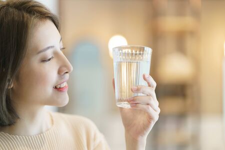 Woman holding transparent glass in her hand and drinking water.