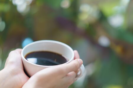 Cup of coffee or tea. White cup of hot beverage in the garden. focus finger