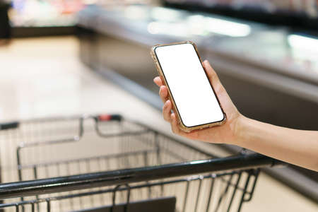 Mockup, hands holding blank white screen mobile phone with shopping cart in supermarket, digital payment conceptの写真素材
