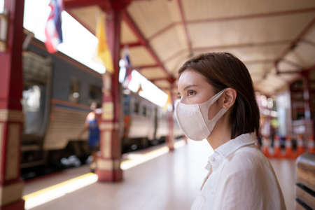 Woman in protective mask wait for the local train on platform at station.の写真素材