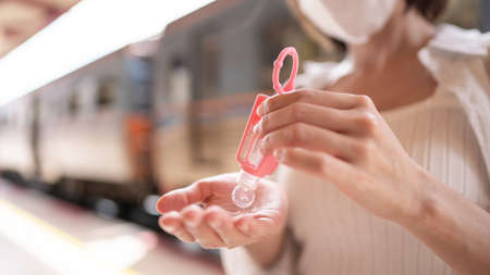 Woman in protective mask using hand sanitizer gel during wait for the local train on platform at...