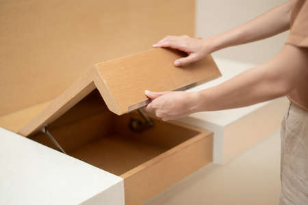 Woman hand opening cupboard of brown wooden table built in.の写真素材