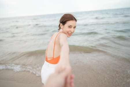 Woman holding her boyfriend hand running together on the beach.の写真素材