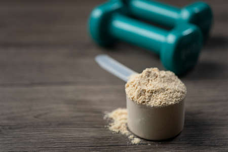 Whey protein powder in scoop and dumbbells. Sports drink, nutrition for muscle growth.の写真素材