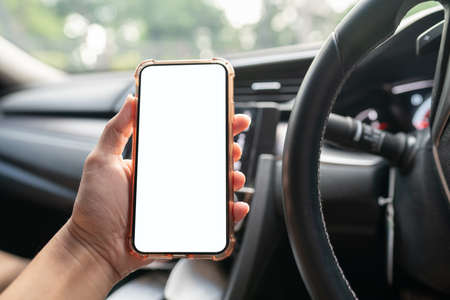 Image of hand holding mobile phone with mockup white screen in car.