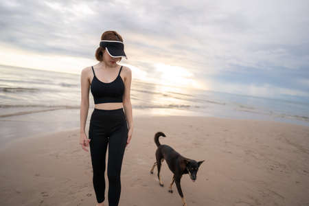 Woman walking along a beach with dog in the morning.の写真素材