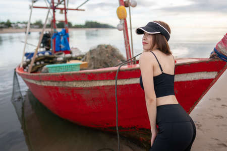 Sporty woman pose with fishing vessel on the beach in the morning.の写真素材