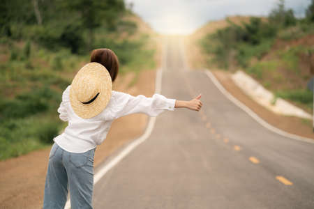 Woman hitchhiking on the road, empty rural curve, asphalt road way. Rear view.の写真素材
