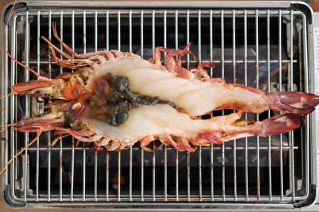 Fresh raw tiger prawn cut in half on gas BBQ grill roaster.