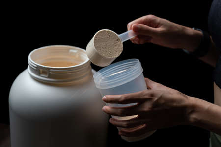 Close up of women with measuring scoop of whey protein, jar and shaker bottle, preparing protein shake.の写真素材