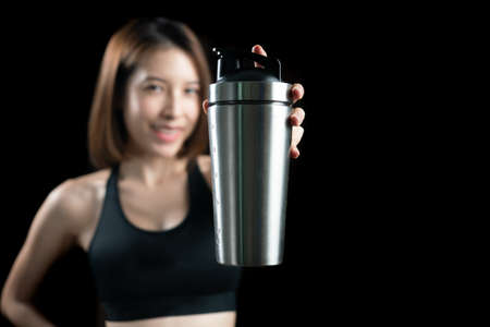 Woman with protein drink in shaker in hand over black background.の写真素材