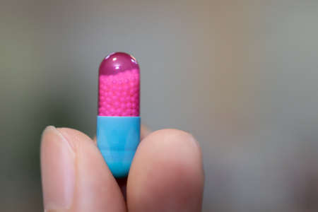 Hand showing blue and pink capsule pill on blurred background