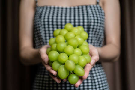 Woman hand holding yellow green bunch of grape.