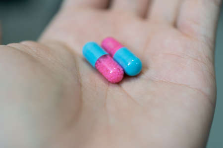 Hand showing blue and pink capsule pill on blurred backgroundの写真素材