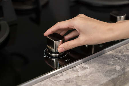 Woman hand turning switch knob on gas stove in kitchen.