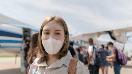 Asian woman wearing protective face mask during covid-19 virus pandemic,  walks to stair entering airplane, parking outside terminal in airport.の写真素材