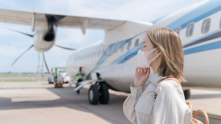 Asian woman wearing protective face mask during covid-19 virus pandemic,  walks to stair entering airplane, parking outside terminal in airport.の写真素材