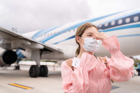 Asian woman wearing protective face mask during covid-19 virus pandemic,  walks to stair entering airplane, parking outside terminal in airport.の写真素材