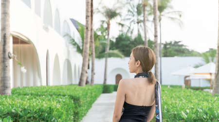 Back view of woman in one piece swimsuit with view on garden and palm trees. Relaxing summer day,...