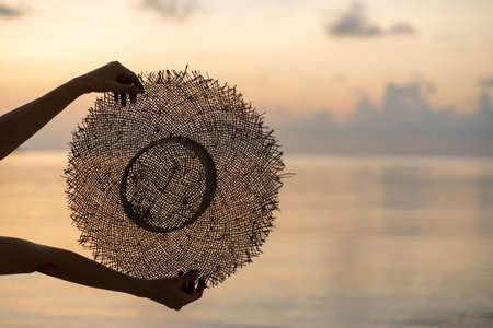 Female hands hold summer straw hat with sunset view. Vacation conceptの写真素材