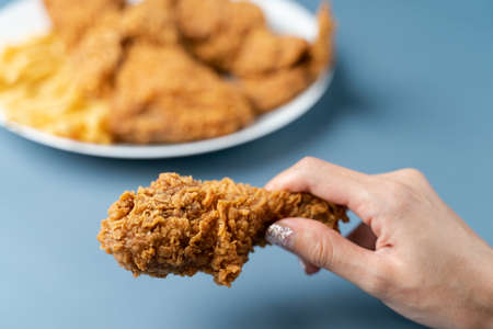 Hand holding drumsticks, crispy fried chicken with french fries in white plate  on blue background.