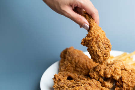 Hand holding drumsticks, crispy fried chicken in white plate on blue background.の写真素材