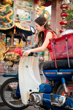 Asian woman wearing red Cheongsam dress pose with classic style shopping motorcycle at China town. Chinese new year concept.の写真素材
