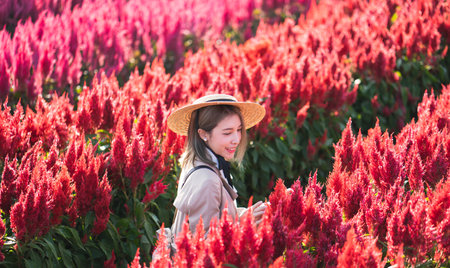 Woman in trench coat and straw hat  in the red flower field.