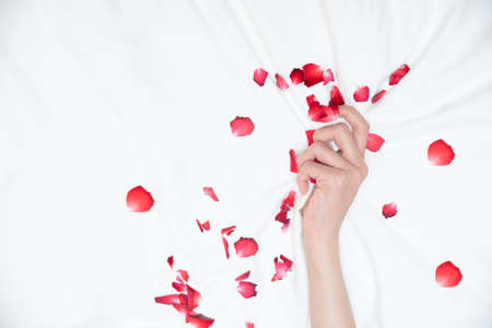 Women hand pulling or grasping white sheets. Hand sign orgasm of woman on white bed sheet with rose...