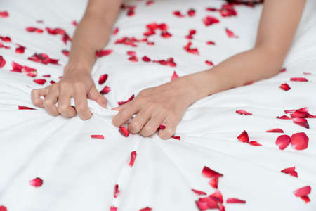 Woman hand grasping white sheet and rose petals. Couple making love or having sex in bedroom.の写真素材