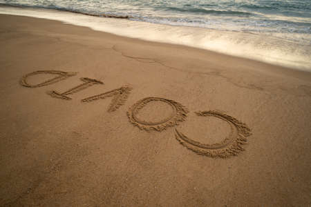 Handwriting COVID on sand and foam wave on beach. Coronavirus concept.の写真素材