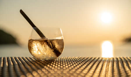 Ice cocktail glasses with cinnamon straws on wooden table over sea sunset.の写真素材