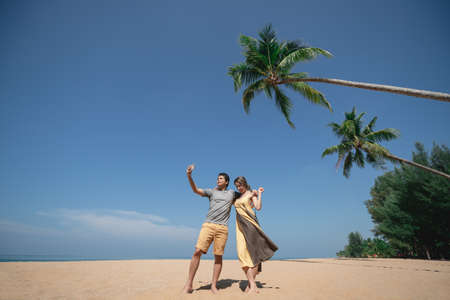 Couple selfie under coconut palm tree on the sandy beach with blue sky.の写真素材