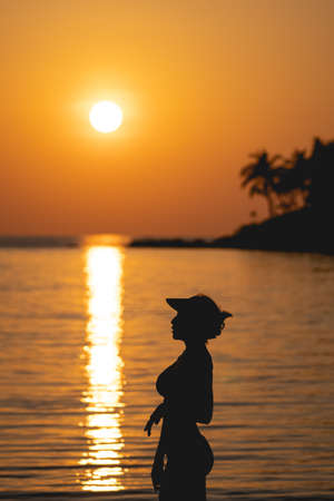 Sunset ocean view. Sun above the sea on orange sky. Woman standing on beach.の写真素材